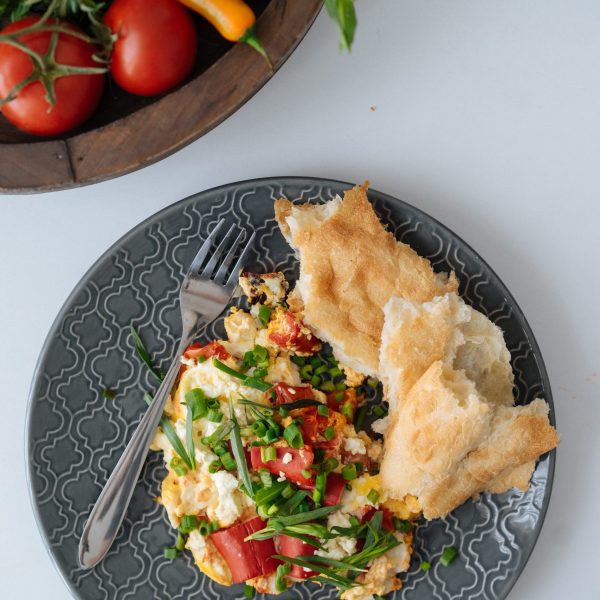 Crop female hands sprinkling with chopped green onion freshly cooked dish with vegetables on ornamented ceramic plates with vegetables and mugs with hot drinks standing on table nearby