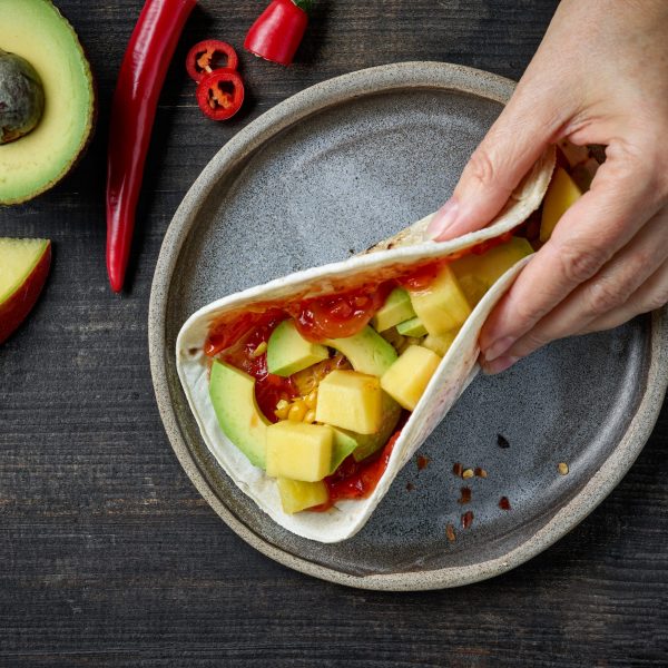 Mexican food tacos in human hand on dark wooden table, top view